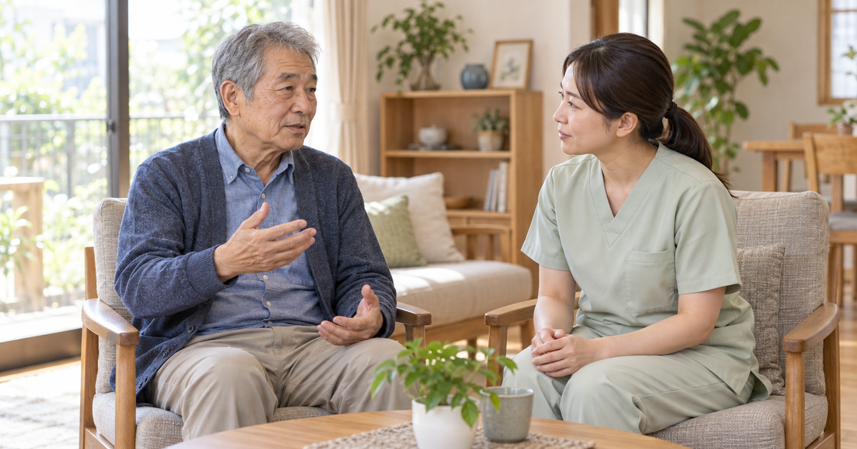 自宅で高齢男性が気持ちを話し、同じ目線に座った女性の専門職が穏やかに耳を傾けている